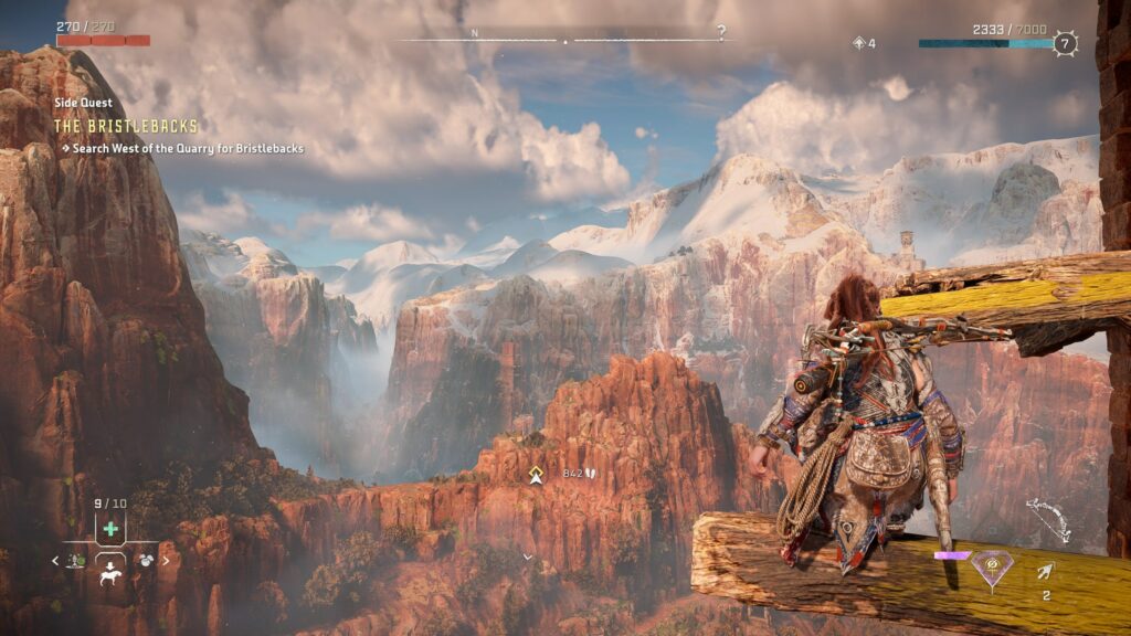 Horizon Forbidden West Complete Edition has amazing vistas and visuals. Alloy sitting on a beam watching over a valley of orange rocks and snowy peaks in the distance.